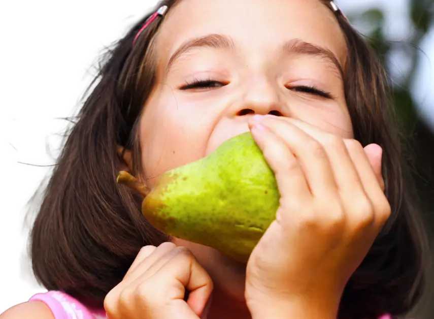 Child joyfully taking a big bite of a green pear outdoors, showing fresh fruit enjoyment and healthy eating for a vibrant and appealing presentation